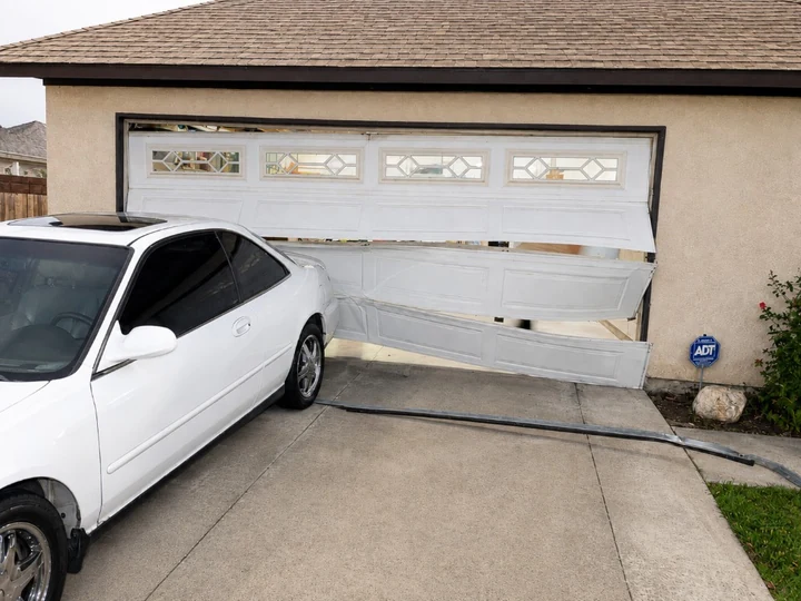 Car crashed through a white sectional garage door, with the door panels and track torn off