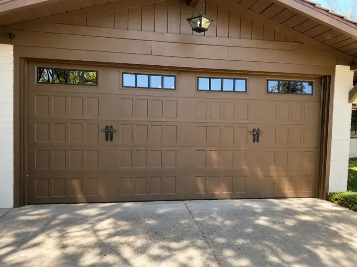 Newly installed brown carriage-style garage door with window inserts and decorative hardware