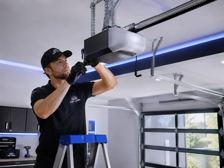 Technician fitting a ceiling-mounted garage door opener unit from a step ladder