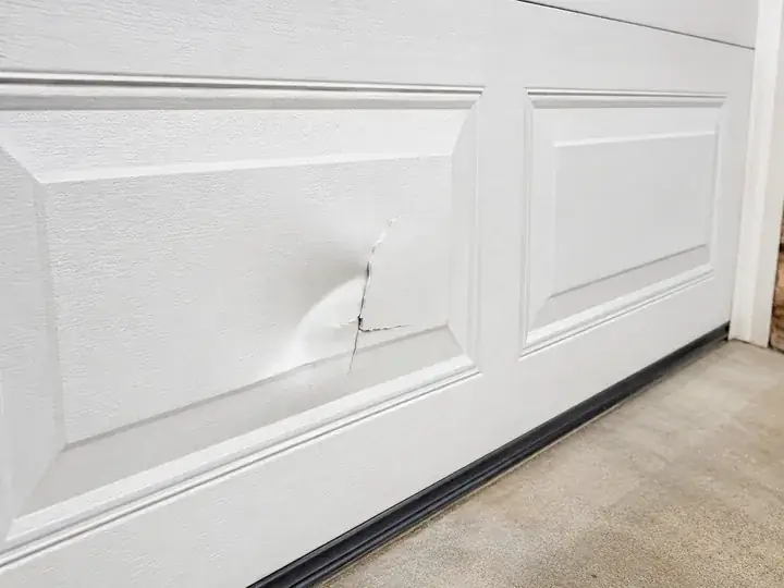 Cracked and dented section on a white raised-panel garage door