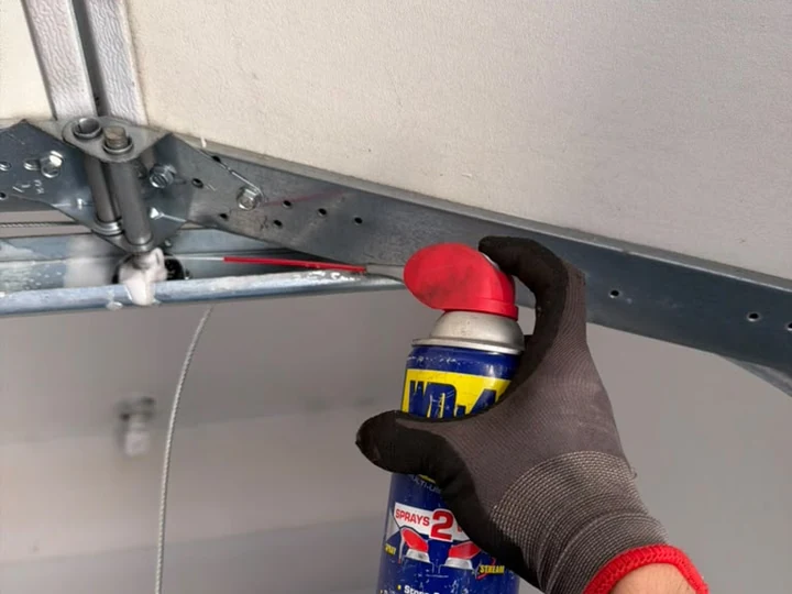 Technician lubricating a garage door hinge and roller during a maintenance visit