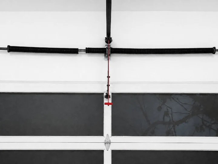 Torsion springs on the spring bar above a white garage door with window inserts